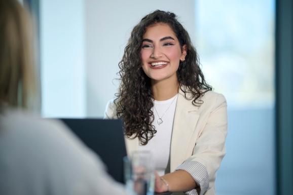 Eda Kurt sitzt vor einem Notebook und lächelt in die Kamera