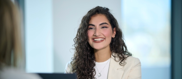 Eda Kurt sits in front of a laptop and smiles at the camera.