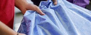 Zwei Personen prüfen sorgfältig die Textur und das Muster eines hochwertigen blauen Damaststoffes.