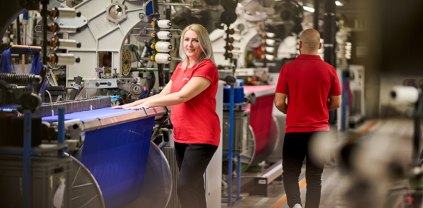 Woman standing at a weaving machine and smiling friendly